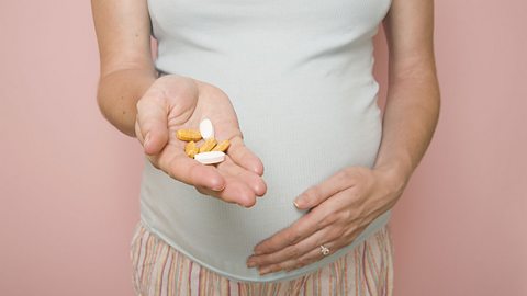 Pregnant woman holding out a handful of vitamin supplement