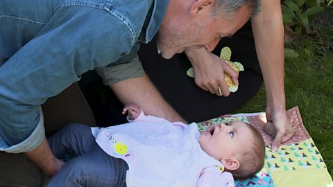 A dad looking at his baby girl on a mat.