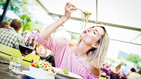 A woman happily eating spaghetti with a fork.