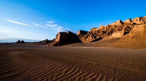 A desert with blue sky, golden brown rocks and sand.