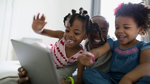 Two toddlers with their dad waving at mobile tablet device