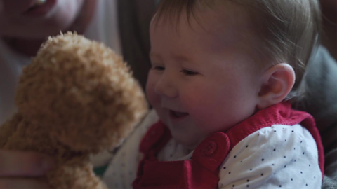 A baby girl smiling at a teddy.