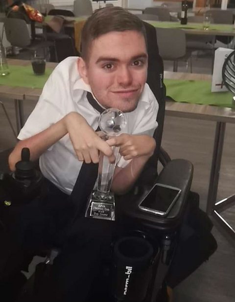 A man in a wheelchair holding a trophy.