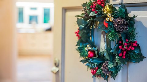 A Christmas wreath with pinecones and holly hanging on a door.