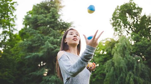 A woman in a park juggling.