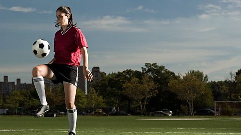 A woman in football kit doing a keepy uppy.