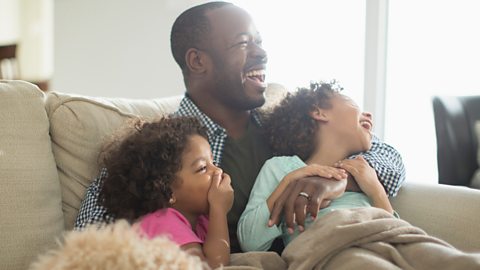 father and two children sit on the sofa laughing together