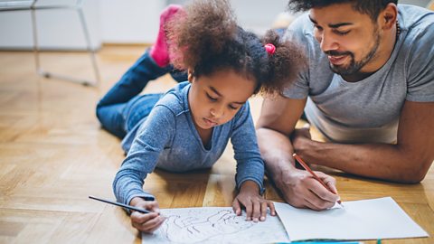 A father and daughter, led on the floor, colouring together