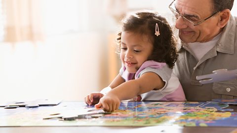 Young girl does a jigsaw with her grandfather