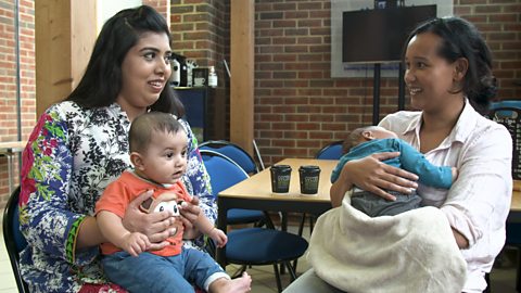 Two mums having a chat with their babies sat on their laps.