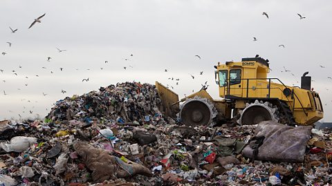 Bulldozer pushing a pile of waste at a landfill site.