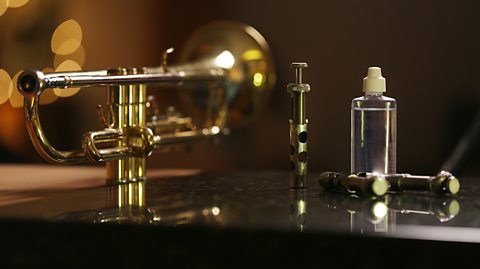 A disassembled trumpet with its finger valves removed and placed at the side with a bottle of oil.