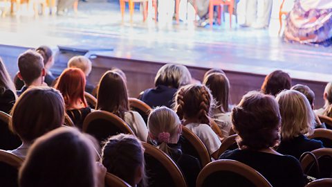 A group of people sit watching a staged performance.