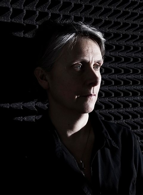 Theatre practitioner Katie Mitchell stands half within shadows against a soundproofed wall.