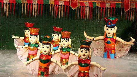 Seven colourful puppets are dancing within water in a traditional Vietnamese water puppet show.