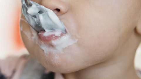 A baby's mouth eating yoghurt.