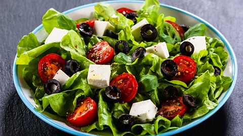 A photo of a salad with lettuce, tomatoes, olives and chunks of feta.