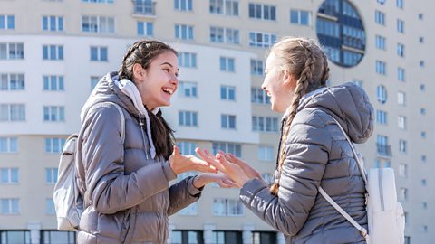 A photo of two girls talking outside a block of flats