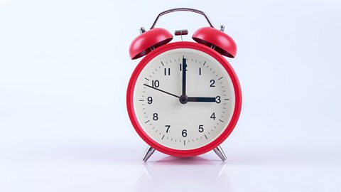 A photo of an analogue alarm clock showing three o'clock