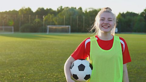 A photo of a teenage girl on a football pitch, holding a football