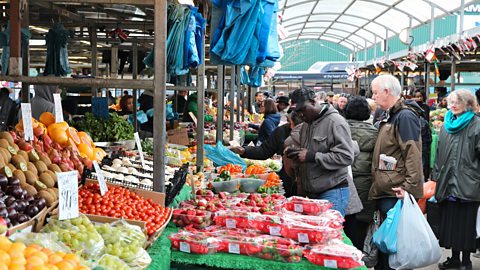 A photo of shoppers at a market vegetable stall