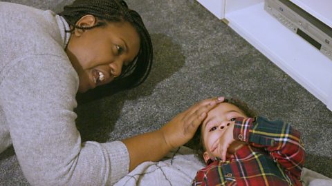 A mum and her son are lying on their carpeted floor. They are halfway through singing Sleeping Bunnies.