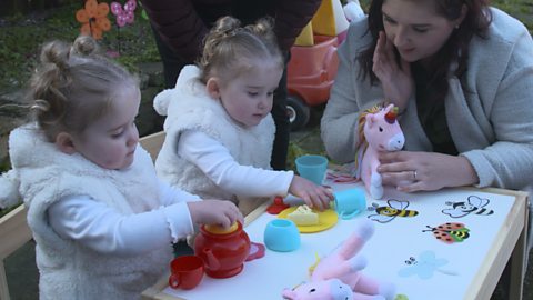 Mum looking on as toddlers have a toy tea party.