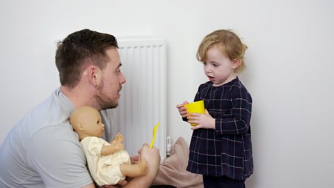 A toddler girl and her dad playing with a doll.