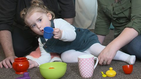 Little girl on the floor holding a blue cup.