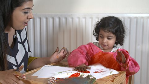 Mum and little daughter sat at table doing finger and hand prints.