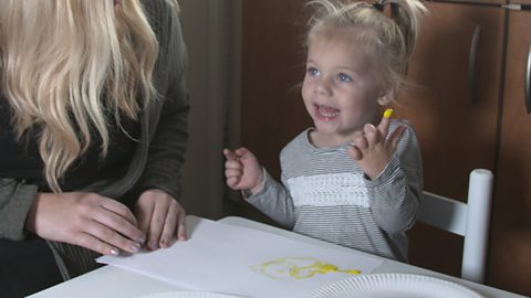 A 2 year old girl with yellow paint on her finger.