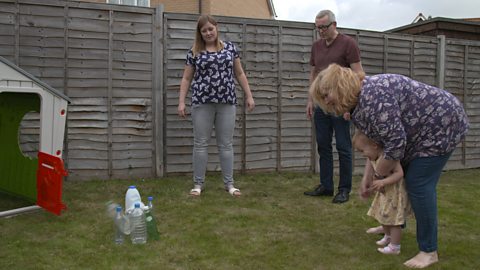 family playing homemade bowling with some plastic bottle skittles on their back garden. 