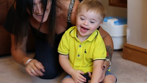 Little boy sat on the living room floor with his mum. 