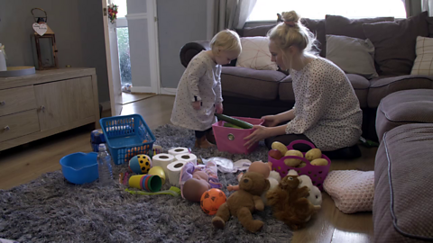 Toddler places cucumber in pink box held by her mum in a shopping game.