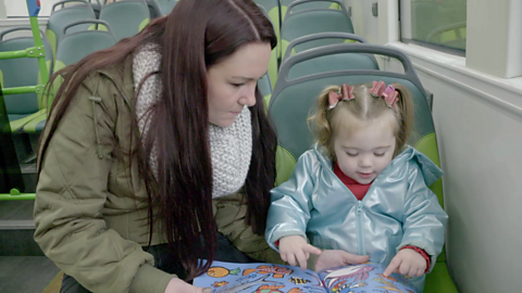 A mum and her little girl looking at a picture book together on the bus.