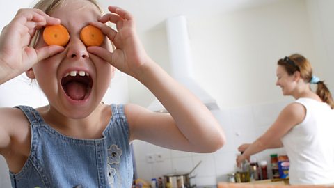 A child holds up chopped carrots to her eyes 