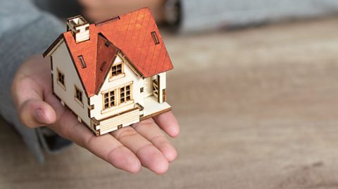 A person's hand holding a model home.