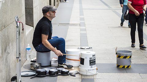 A street performer plays a drum kit made from buckets and pans.