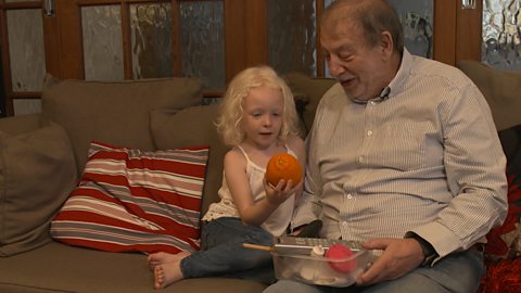 Little girl and granddad on the sofa, holding an orange.