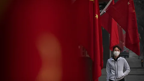 Getty Images A young woman wearing a mask walks past Chinese flags (Credit: Getty Images)