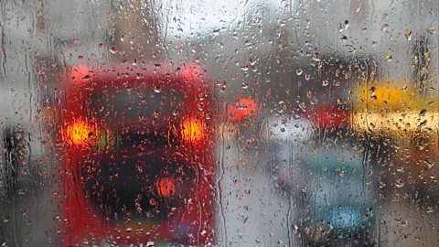 A glass plane blurred by rain in traffic.