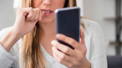 A woman biting her nails and playing on her phone.