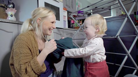 Mum and toddler holding clothes next to laundry airer