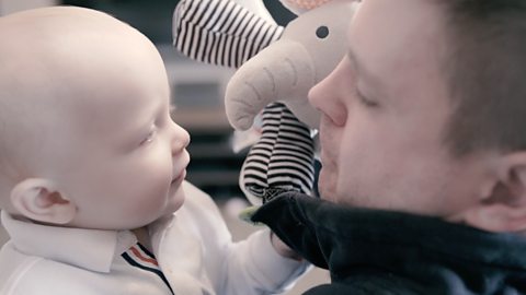 A dad and his baby playing hide and seek with a toy elephant. 