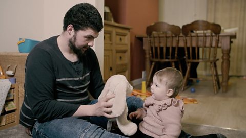 A dad playing with a teddy bunny rabbit with his baby daughter.