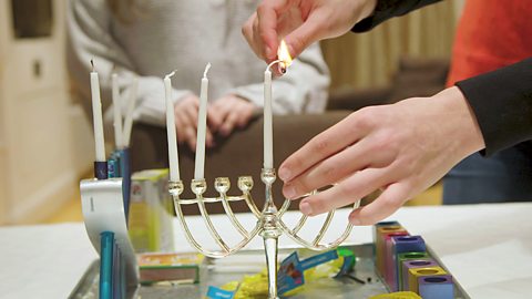 Zack is lighting the shamash candle on his family's hanukkiah.