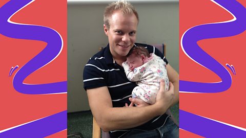 Simon King sat on chair holding his newborn baby Nell