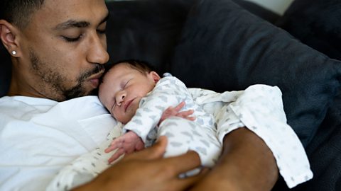 Dad lying on sofa kissing his tiny baby