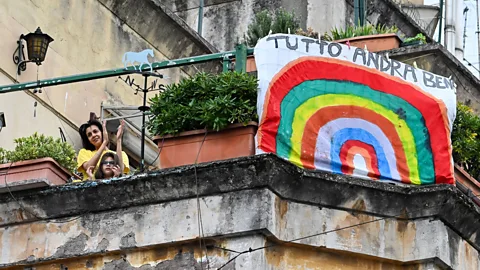 Getty Images Italians wave next to a banner reading "Tutto Andra Bene" (everything will be OK) (Credit: Getty Images)