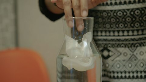 Elle dropping a wet wipe into a vase of water.